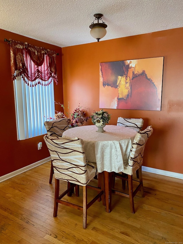 dining area with a textured ceiling, hardwood / wood-style flooring, and baseboards