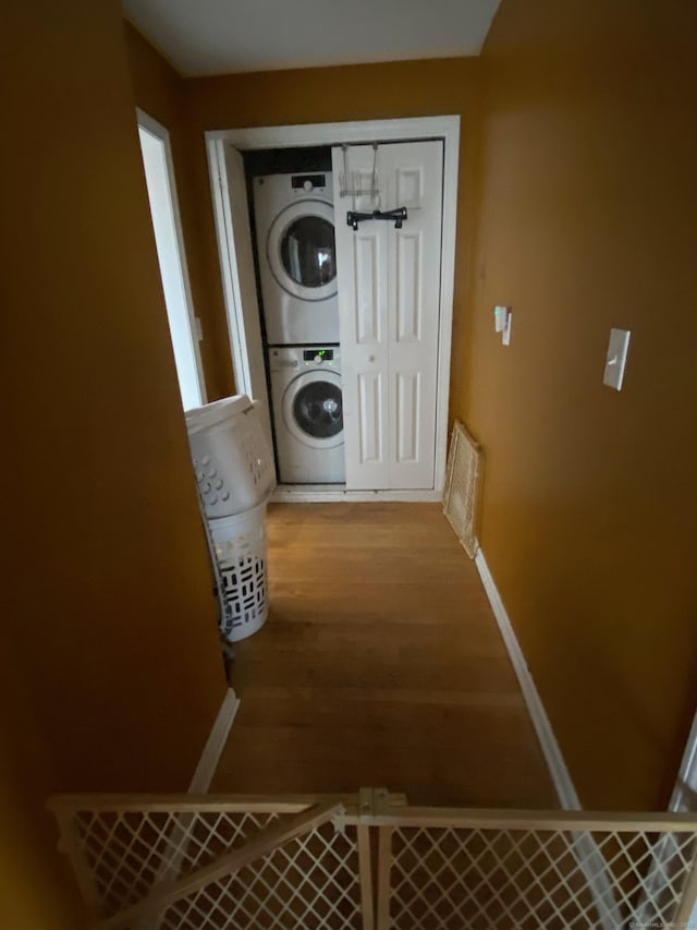 laundry area featuring stacked washer and dryer, laundry area, baseboards, and wood finished floors