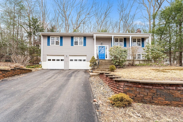 bi-level home featuring covered porch, aphalt driveway, a chimney, and a garage