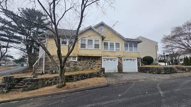 view of front of home with a garage, stairs, driveway, stone siding, and stucco siding