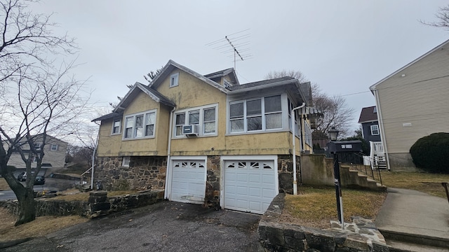 view of front of house featuring stucco siding, an attached garage, cooling unit, stone siding, and driveway