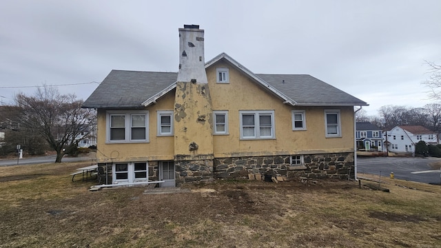 back of property with roof with shingles, a chimney, and stucco siding