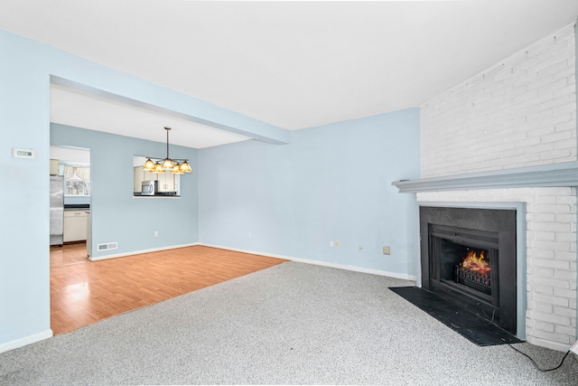 carpeted living room featuring a brick fireplace, wood finished floors, an inviting chandelier, and baseboards