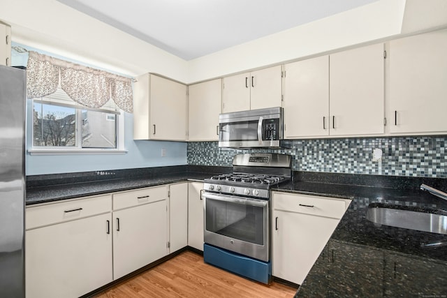 kitchen featuring light wood-style flooring, a sink, appliances with stainless steel finishes, dark stone counters, and tasteful backsplash