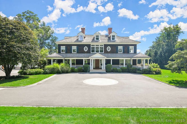 shingle-style home featuring aphalt driveway, a porch, and a front yard