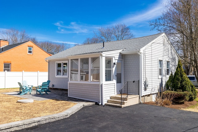 view of front of property with a patio area, a shingled roof, a sunroom, and fence