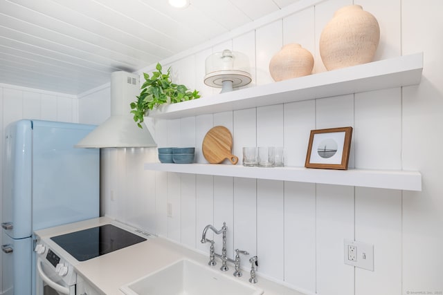 kitchen with oven, open shelves, a sink, wall chimney range hood, and light countertops