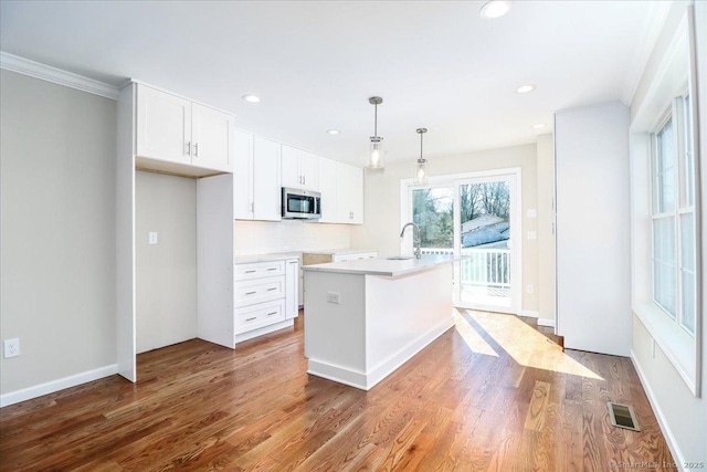 kitchen with visible vents, white cabinets, stainless steel microwave, wood finished floors, and a sink