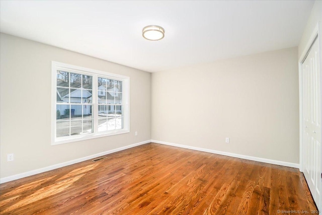 empty room with wood finished floors, visible vents, and baseboards