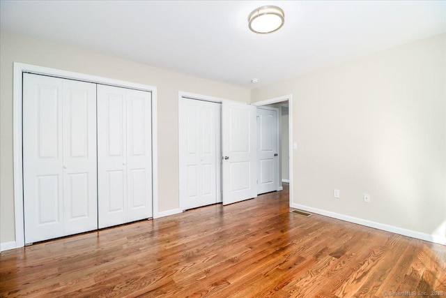 unfurnished bedroom with baseboards, visible vents, light wood-style flooring, and multiple closets