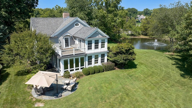 rear view of property with a lawn, a chimney, roof with shingles, a water view, and a patio area