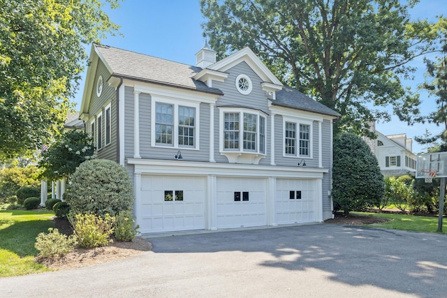 view of side of property with a garage, driveway, a chimney, and roof with shingles