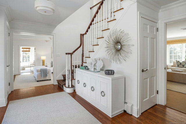 corridor with a baseboard heating unit, ornamental molding, dark wood-type flooring, and stairway