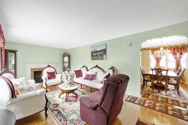 living area with arched walkways, a fireplace, an inviting chandelier, and wood finished floors