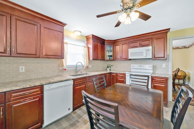 kitchen with backsplash, glass insert cabinets, light stone counters, white appliances, and a sink