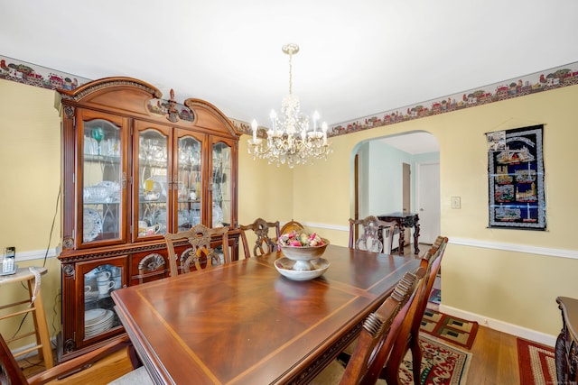 dining area with arched walkways, a chandelier, baseboards, and wood finished floors