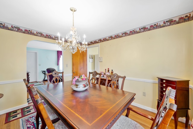 dining room featuring a notable chandelier, arched walkways, light wood-style floors, and baseboards