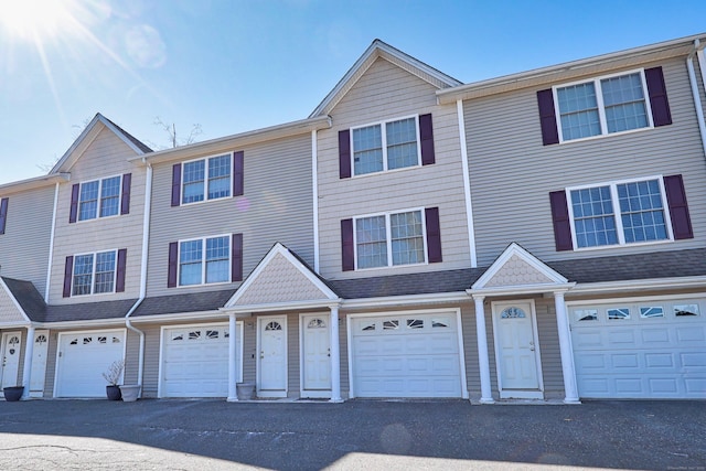 multi unit property featuring an attached garage, driveway, and a shingled roof