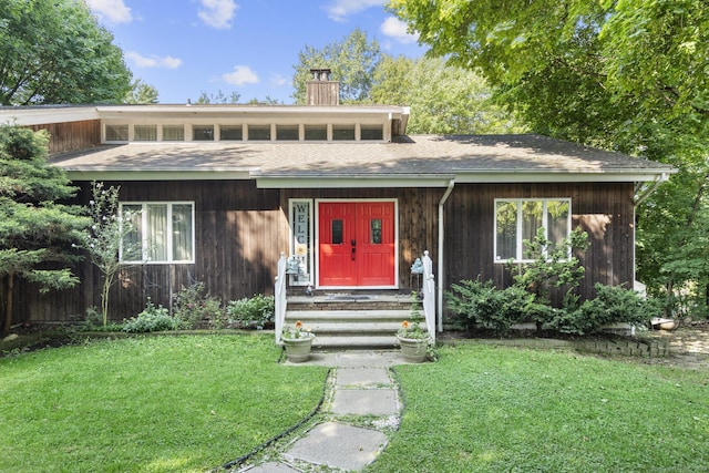 view of front facade featuring a shingled roof, a front yard, and a chimney