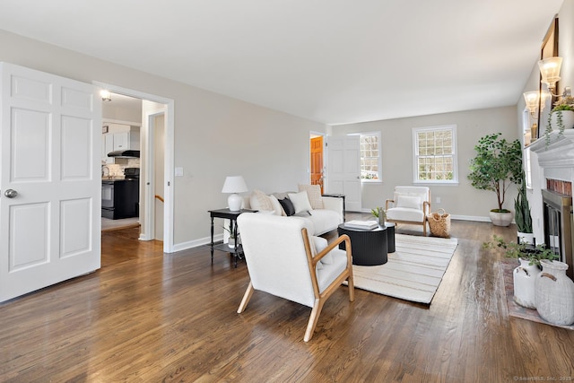 living room featuring a brick fireplace, baseboards, and wood finished floors