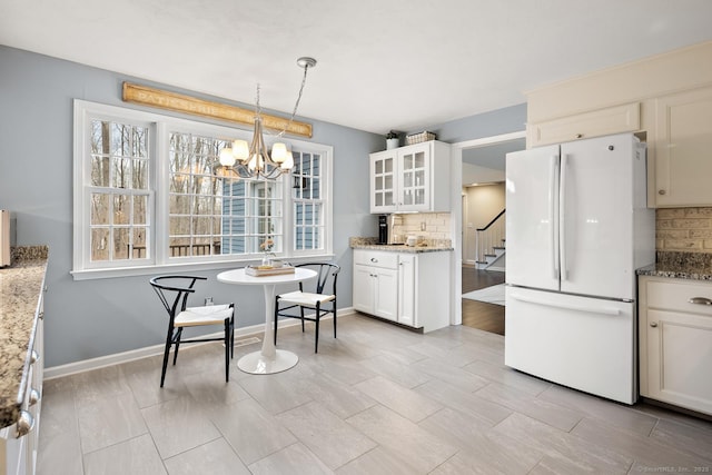 kitchen featuring glass insert cabinets, freestanding refrigerator, decorative backsplash, and light stone countertops