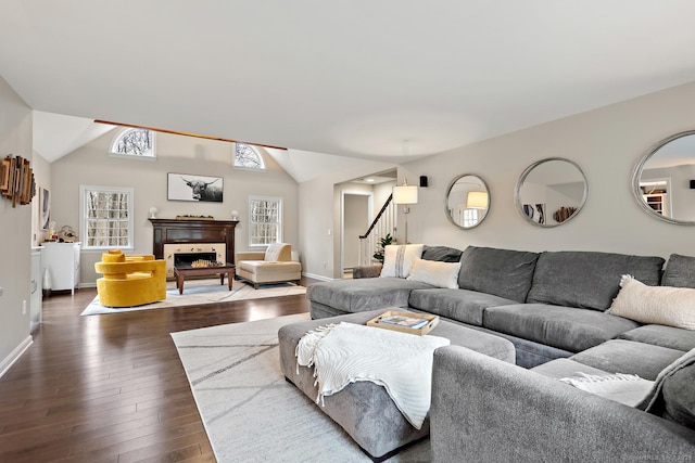 living room featuring dark wood-style floors, lofted ceiling, a fireplace, and baseboards