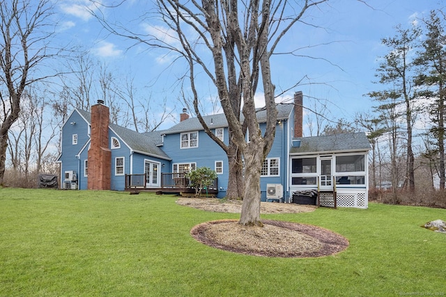 rear view of property featuring a deck, a lawn, a chimney, and a sunroom