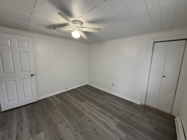 unfurnished bedroom with ceiling fan, brick wall, a closet, baseboard heating, and dark wood finished floors