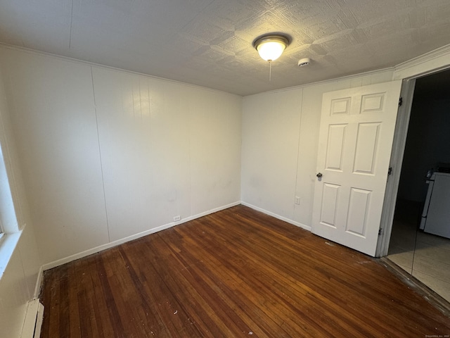 empty room featuring washer / clothes dryer, baseboard heating, hardwood / wood-style flooring, and baseboards