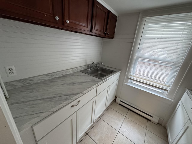 kitchen featuring light stone counters, light tile patterned flooring, a baseboard heating unit, a sink, and white cabinets