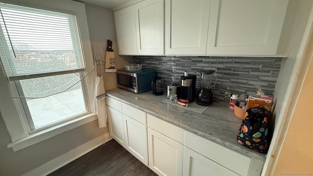 bar with dark wood-style flooring, stainless steel microwave, backsplash, and baseboards