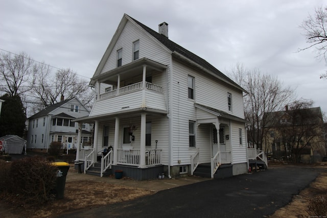 view of front of home featuring a balcony, covered porch, and a chimney