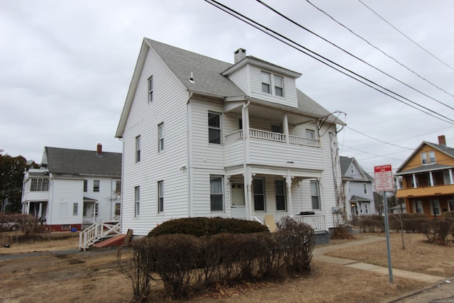 view of front of home with covered porch, a chimney, a balcony, and a shingled roof