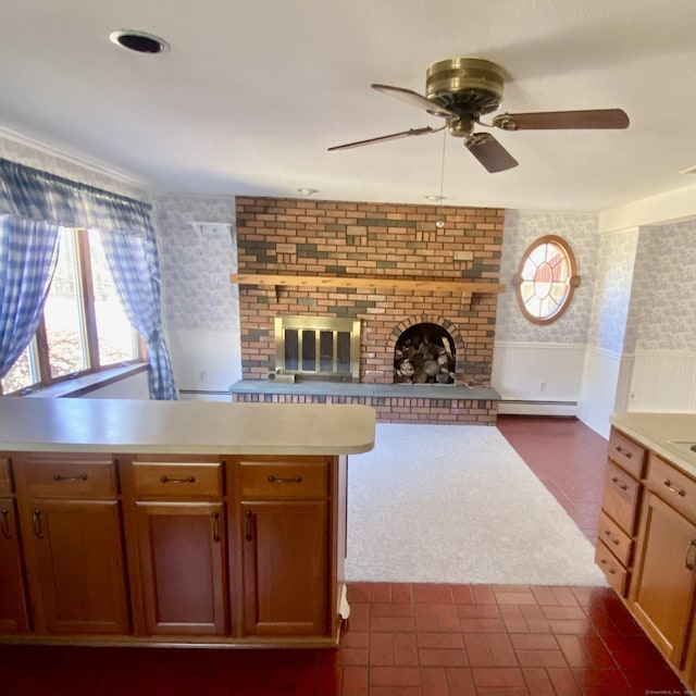 kitchen with brick floor, a fireplace, light countertops, baseboard heating, and wainscoting