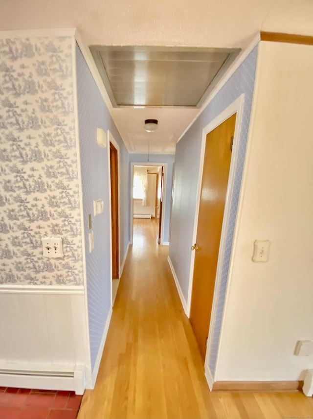 corridor with wallpapered walls, attic access, light wood finished floors, wainscoting, and baseboard heating