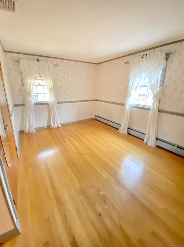 additional living space featuring a healthy amount of sunlight, wood finished floors, visible vents, and wallpapered walls