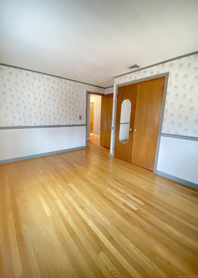 unfurnished room featuring a wainscoted wall, light wood-style floors, and wallpapered walls