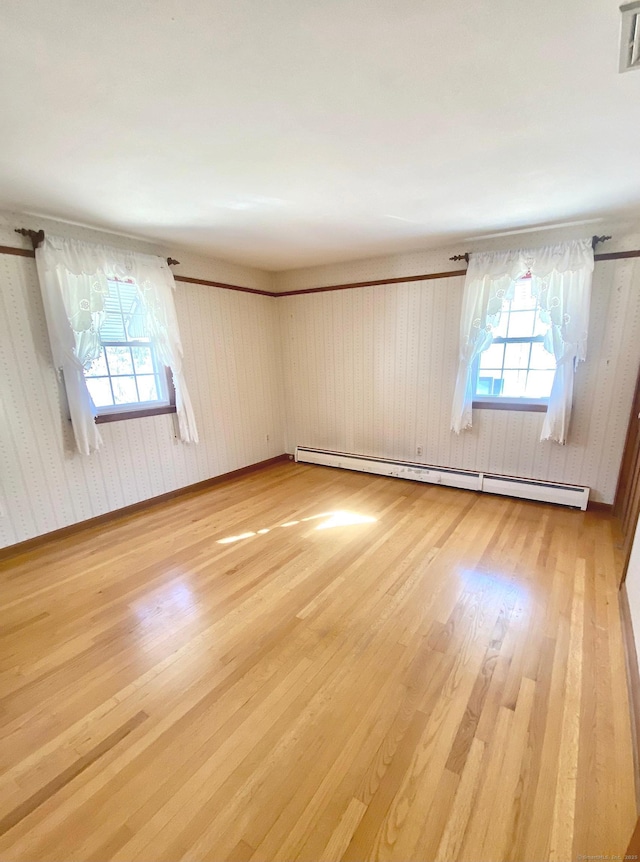 spare room with a baseboard heating unit, light wood-type flooring, a wealth of natural light, and baseboards