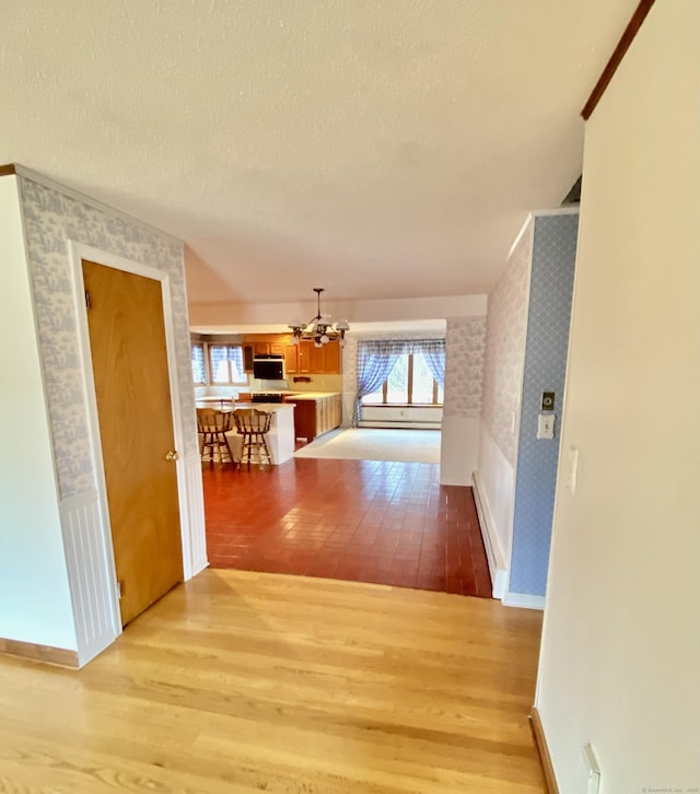 hallway with an accent wall, a textured ceiling, wood finished floors, baseboards, and wallpapered walls