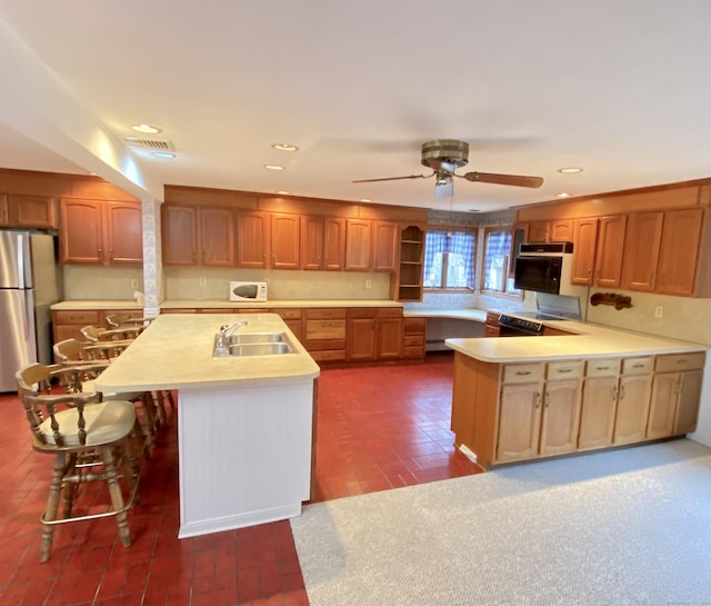 kitchen featuring white microwave, freestanding refrigerator, a peninsula, light countertops, and a sink