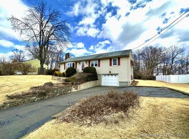 ranch-style home featuring a garage, a chimney, aphalt driveway, fence, and a front yard