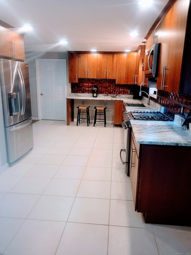 kitchen featuring light tile patterned floors, stainless steel appliances, a sink, brown cabinets, and tasteful backsplash