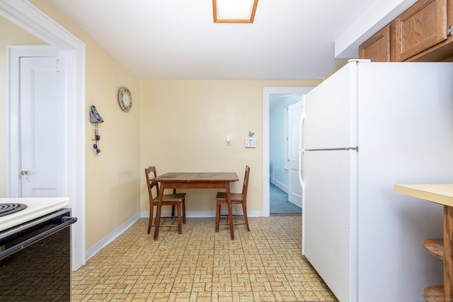 kitchen with baseboards, stove, brown cabinetry, and freestanding refrigerator