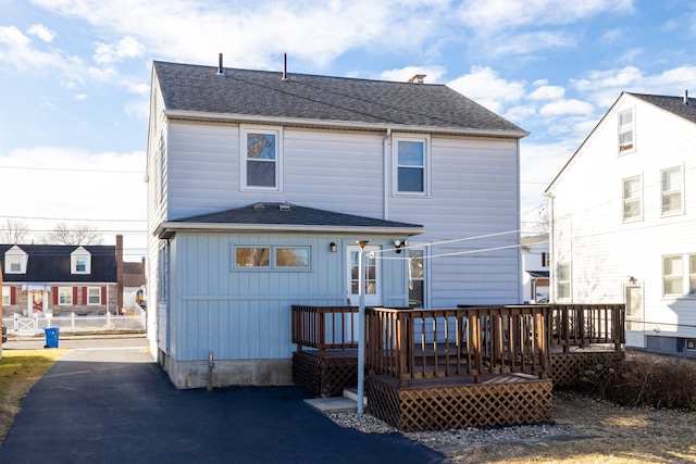 rear view of property with board and batten siding, roof with shingles, and a deck