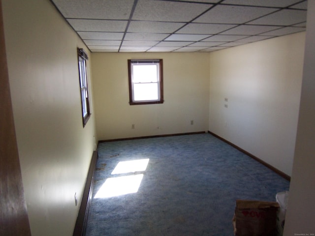 spare room with baseboards, a drop ceiling, and carpet flooring