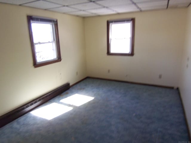 empty room with carpet floors, a drop ceiling, and a baseboard heating unit