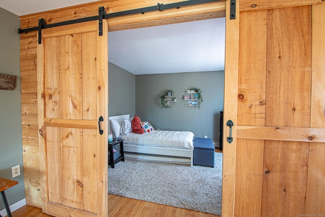 bedroom featuring lofted ceiling, a barn door, baseboards, and wood finished floors