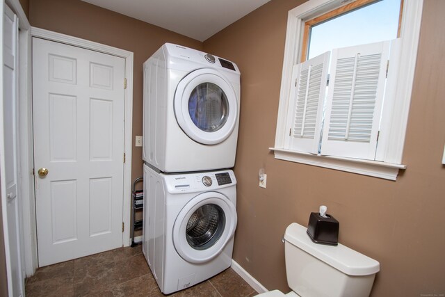 clothes washing area with stacked washer and dryer and baseboards