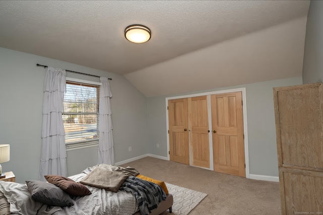 bedroom featuring baseboards, light colored carpet, lofted ceiling, a textured ceiling, and a closet