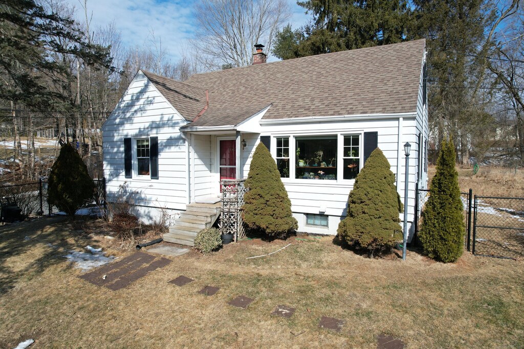 view of front of property featuring a front yard, roof with shingles, fence, and a chimney